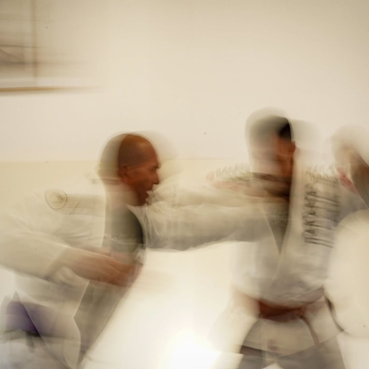 Two jiu-jitsu students in white gis gripping each other mid-exchange, blurred with motion
